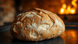 Nahaufnahme von rustikalem Artisanbrot mit goldener Kruste auf einer dunklen Stahloberfläche, warmes Ofenlicht, das die Textur und Wärme hervorhebt.